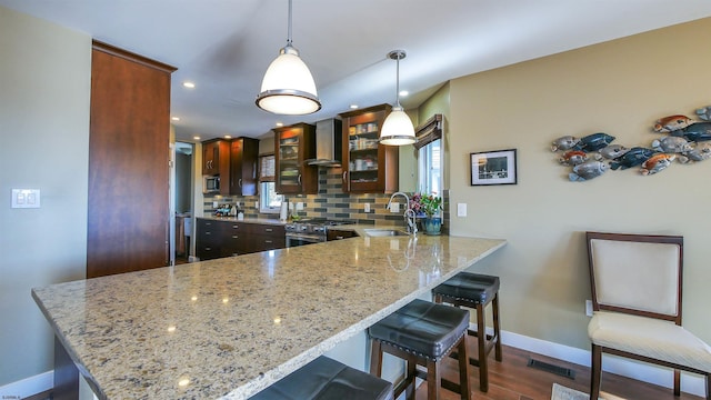 kitchen featuring kitchen peninsula, backsplash, pendant lighting, wall chimney exhaust hood, and sink