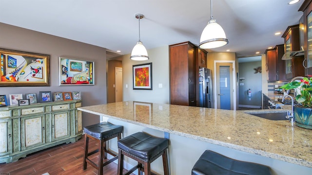 kitchen with pendant lighting, kitchen peninsula, a kitchen bar, sink, and light stone countertops