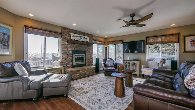 living room with ceiling fan, wood-type flooring, and a stone fireplace