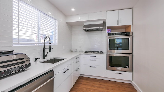 kitchen featuring wall chimney exhaust hood, dark hardwood / wood-style flooring, white cabinetry, appliances with stainless steel finishes, and sink