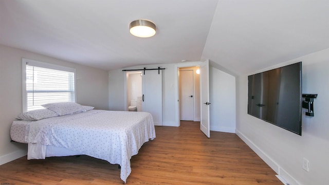 bedroom featuring ensuite bathroom, a barn door, lofted ceiling, and hardwood / wood-style flooring