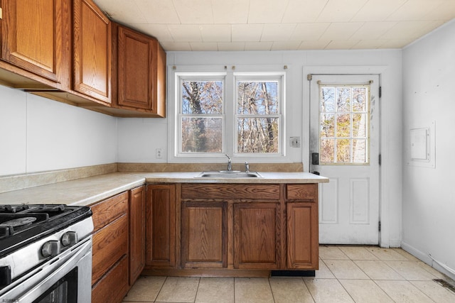 kitchen featuring sink, light tile patterned flooring, and stainless steel gas range oven