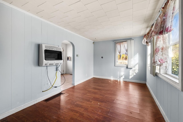 spare room featuring wood-type flooring, a healthy amount of sunlight, heating unit, and crown molding