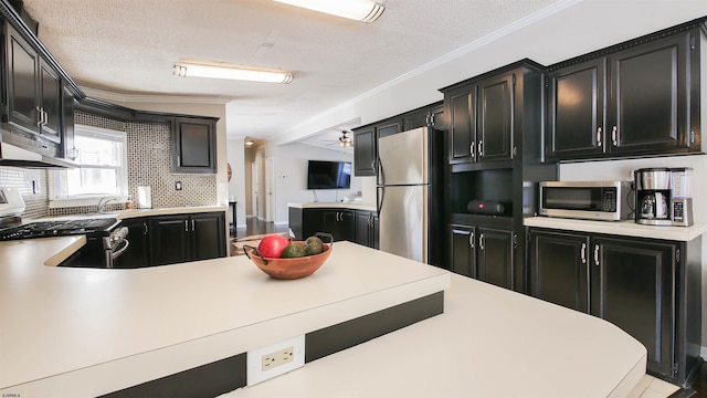 kitchen featuring a textured ceiling, lofted ceiling, backsplash, crown molding, and appliances with stainless steel finishes