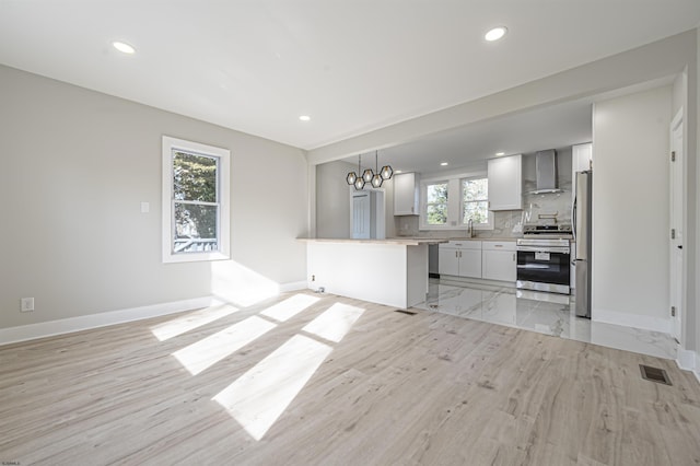 kitchen featuring wall chimney exhaust hood, decorative light fixtures, tasteful backsplash, white cabinetry, and appliances with stainless steel finishes