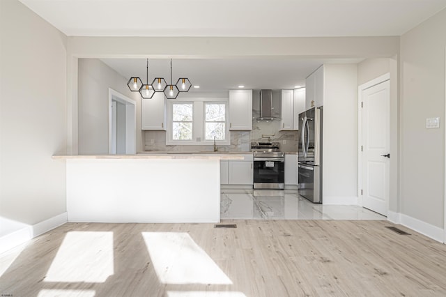 kitchen featuring a chandelier, appliances with stainless steel finishes, hanging light fixtures, wall chimney exhaust hood, and tasteful backsplash