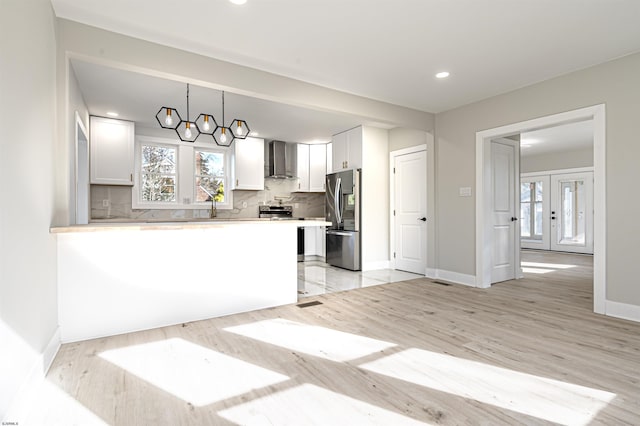 kitchen with wall chimney exhaust hood, a chandelier, decorative light fixtures, tasteful backsplash, and stainless steel refrigerator