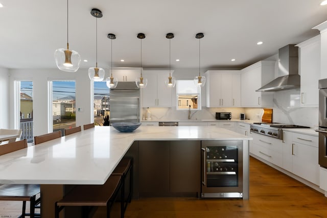 kitchen with wine cooler, a breakfast bar, pendant lighting, a spacious island, and wall chimney range hood