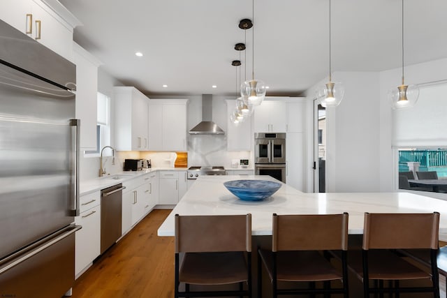 kitchen featuring stainless steel appliances, a spacious island, wall chimney range hood, and hanging light fixtures