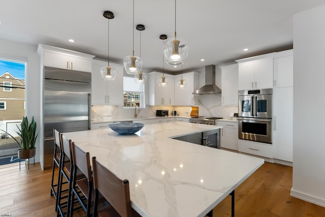 kitchen with a large island, stainless steel appliances, pendant lighting, white cabinetry, and wall chimney range hood