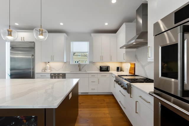 kitchen with white cabinets, appliances with stainless steel finishes, wall chimney exhaust hood, and hanging light fixtures