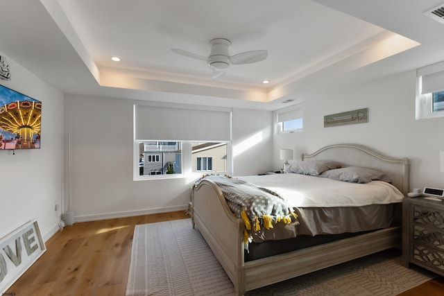 bedroom with ceiling fan, light hardwood / wood-style flooring, and a raised ceiling