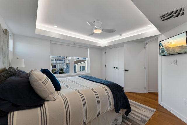 bedroom featuring a raised ceiling, ceiling fan, a closet, and hardwood / wood-style floors