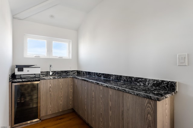 kitchen with dark hardwood / wood-style floors, lofted ceiling, wine cooler, dark stone counters, and sink