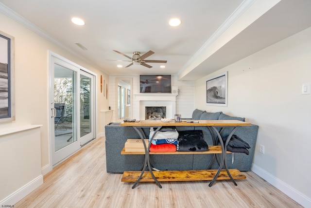 living room featuring light hardwood / wood-style floors, ceiling fan, a large fireplace, and ornamental molding