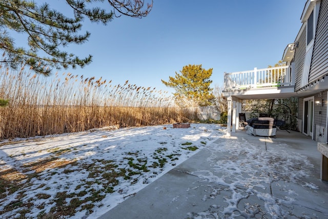 snowy yard featuring a balcony, a patio, and a fire pit