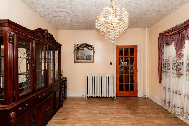 hallway with a textured ceiling, radiator heating unit, a chandelier, and light hardwood / wood-style floors