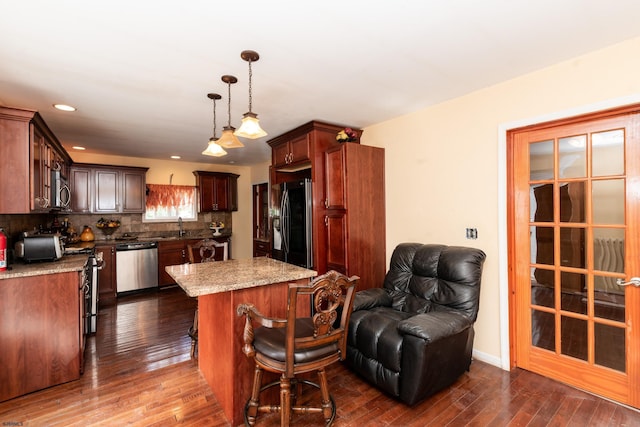 kitchen featuring stainless steel appliances, a center island, dark wood-type flooring, decorative light fixtures, and tasteful backsplash