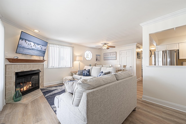 living room featuring ceiling fan, light wood-type flooring, a tile fireplace, and crown molding