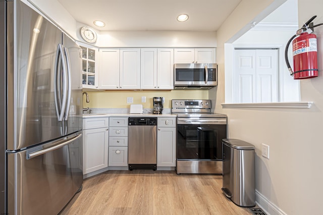 kitchen with stainless steel appliances, white cabinetry, sink, and light hardwood / wood-style floors