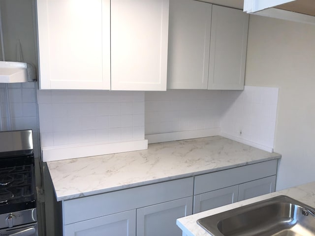 kitchen featuring light stone counters, white cabinets, sink, and decorative backsplash