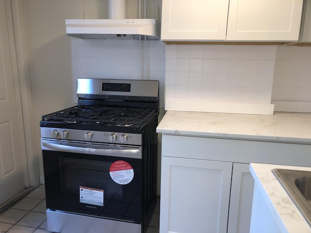 kitchen featuring light stone countertops, stainless steel gas range oven, light tile patterned floors, and white cabinetry