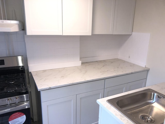 kitchen featuring sink, white cabinetry, stainless steel gas range oven, decorative backsplash, and light stone countertops