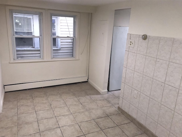 empty room with tile walls, light tile patterned flooring, and a baseboard heating unit