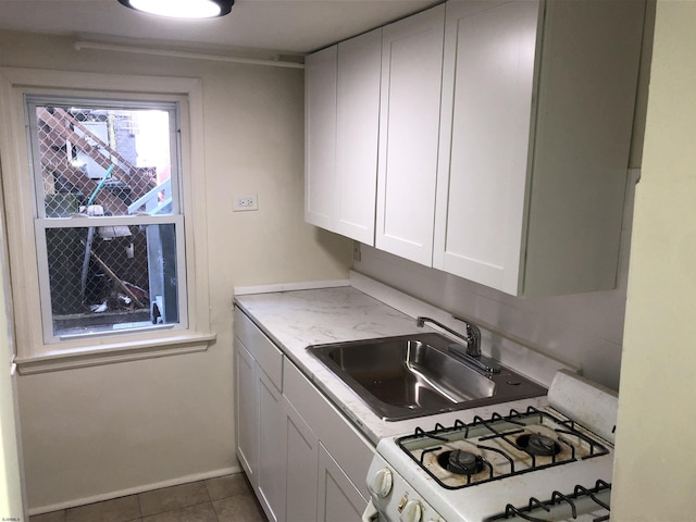 kitchen with sink, white cabinetry, dark tile patterned flooring, and white gas stove