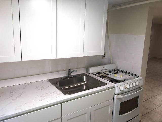 kitchen with white gas range oven, light stone counters, sink, white cabinetry, and backsplash