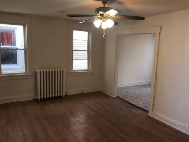 empty room featuring radiator, ceiling fan, plenty of natural light, and dark hardwood / wood-style floors