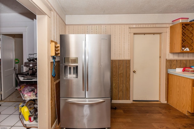 kitchen with stainless steel fridge, wood walls, and a textured ceiling