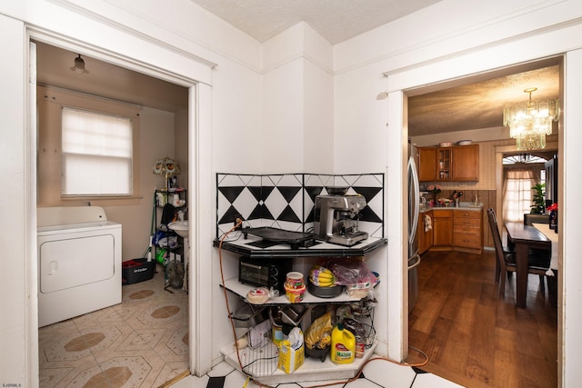 kitchen with washer / dryer, tasteful backsplash, a notable chandelier, dark wood-type flooring, and stainless steel refrigerator