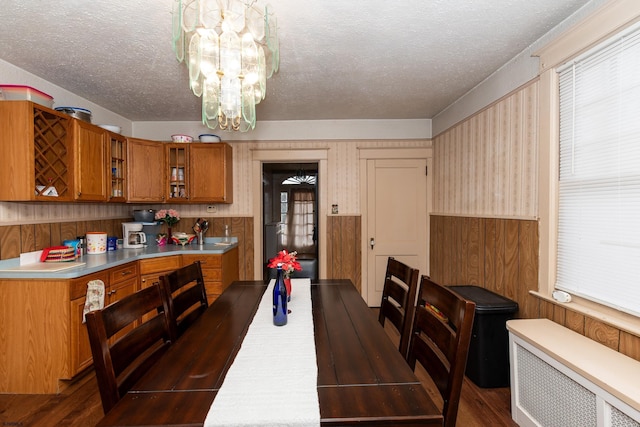 dining room featuring a notable chandelier, a textured ceiling, wood walls, and radiator heating unit