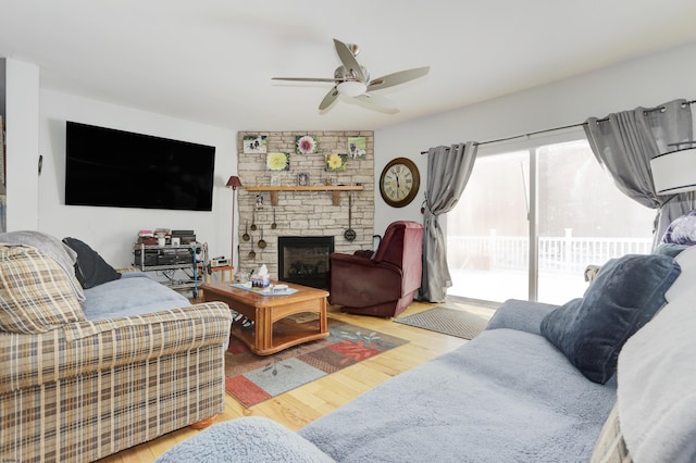 living room with ceiling fan, a stone fireplace, and light wood-type flooring