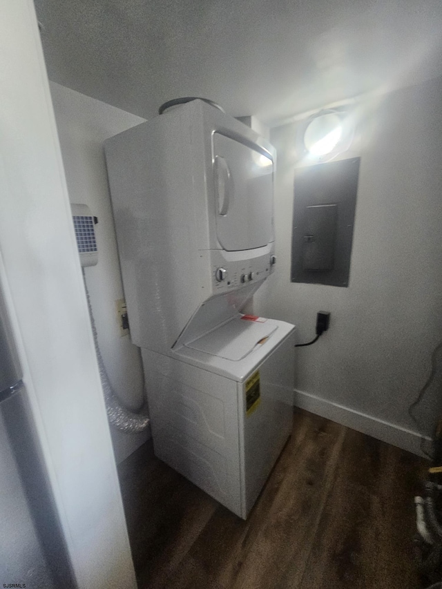 laundry area featuring dark wood-type flooring, electric panel, and stacked washer / dryer