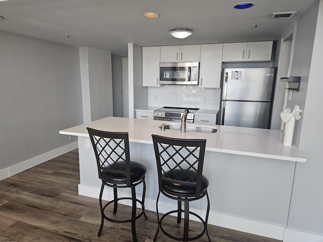 kitchen featuring white cabinetry, stainless steel appliances, decorative backsplash, sink, and a breakfast bar area