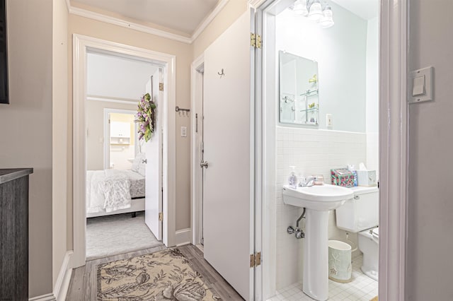 bathroom featuring toilet, tile walls, wood-type flooring, ornamental molding, and sink