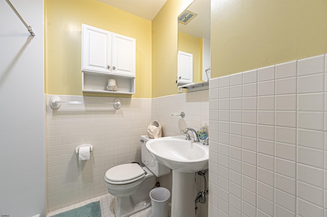 bathroom with toilet, tile walls, and tile patterned floors