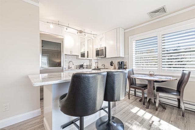 kitchen featuring a kitchen bar, backsplash, white cabinetry, and light hardwood / wood-style flooring