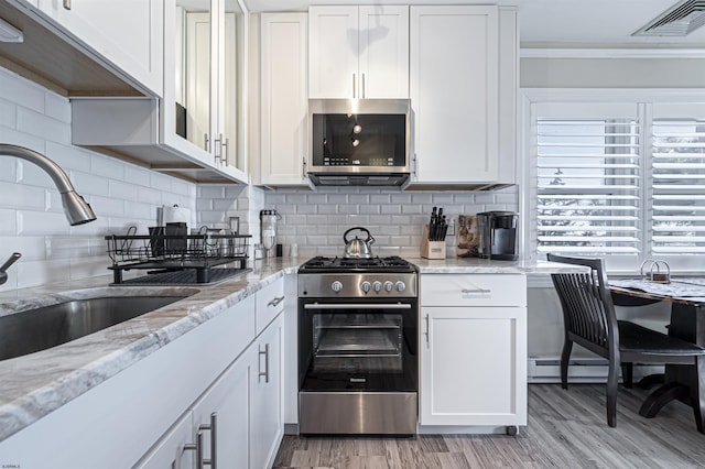 kitchen featuring light wood-type flooring, white cabinetry, stainless steel appliances, and tasteful backsplash