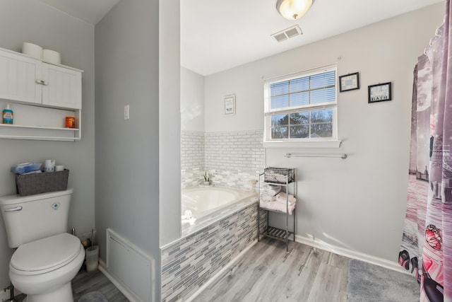 bathroom with tiled bath, toilet, and hardwood / wood-style floors