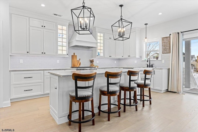 kitchen featuring decorative light fixtures, white cabinets, light stone counters, and a kitchen island