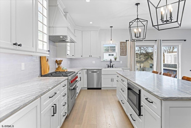 kitchen with white cabinets, appliances with stainless steel finishes, a kitchen island, premium range hood, and backsplash