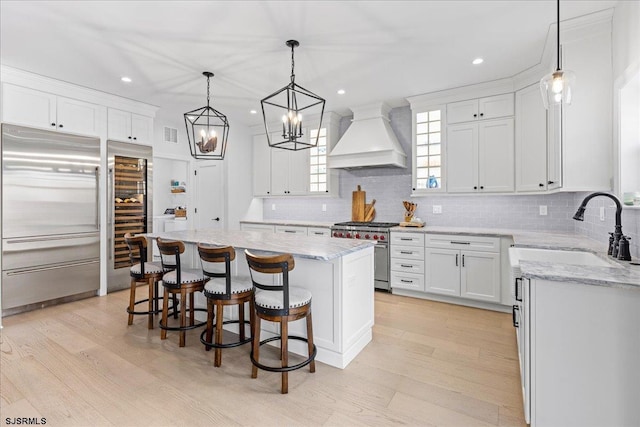 kitchen featuring a kitchen island, white cabinetry, high end appliances, sink, and custom range hood