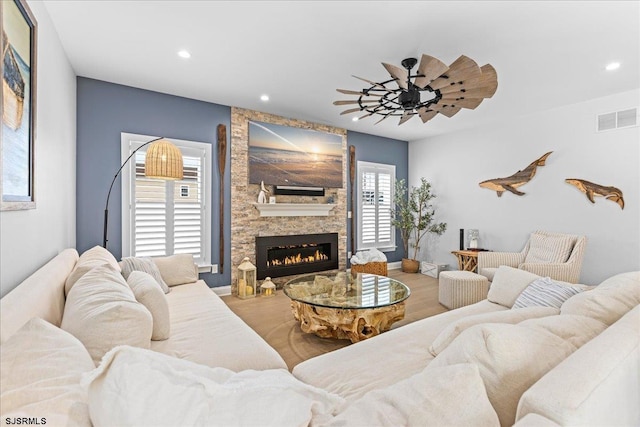 living room with ceiling fan, a stone fireplace, and hardwood / wood-style flooring