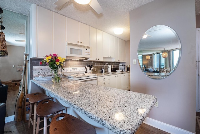 kitchen with white appliances, white cabinetry, tasteful backsplash, sink, and kitchen peninsula