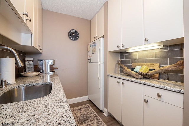 kitchen with white cabinets, white fridge, decorative backsplash, sink, and light stone counters