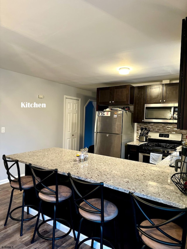 kitchen with light stone countertops, appliances with stainless steel finishes, dark hardwood / wood-style flooring, and a breakfast bar area