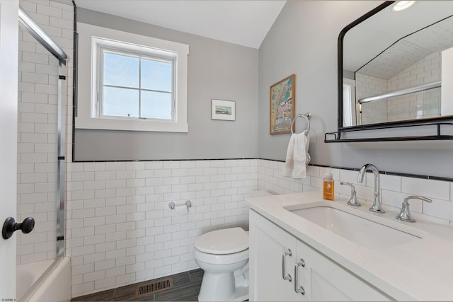 full bathroom featuring tiled shower / bath, vanity, tile walls, toilet, and vaulted ceiling